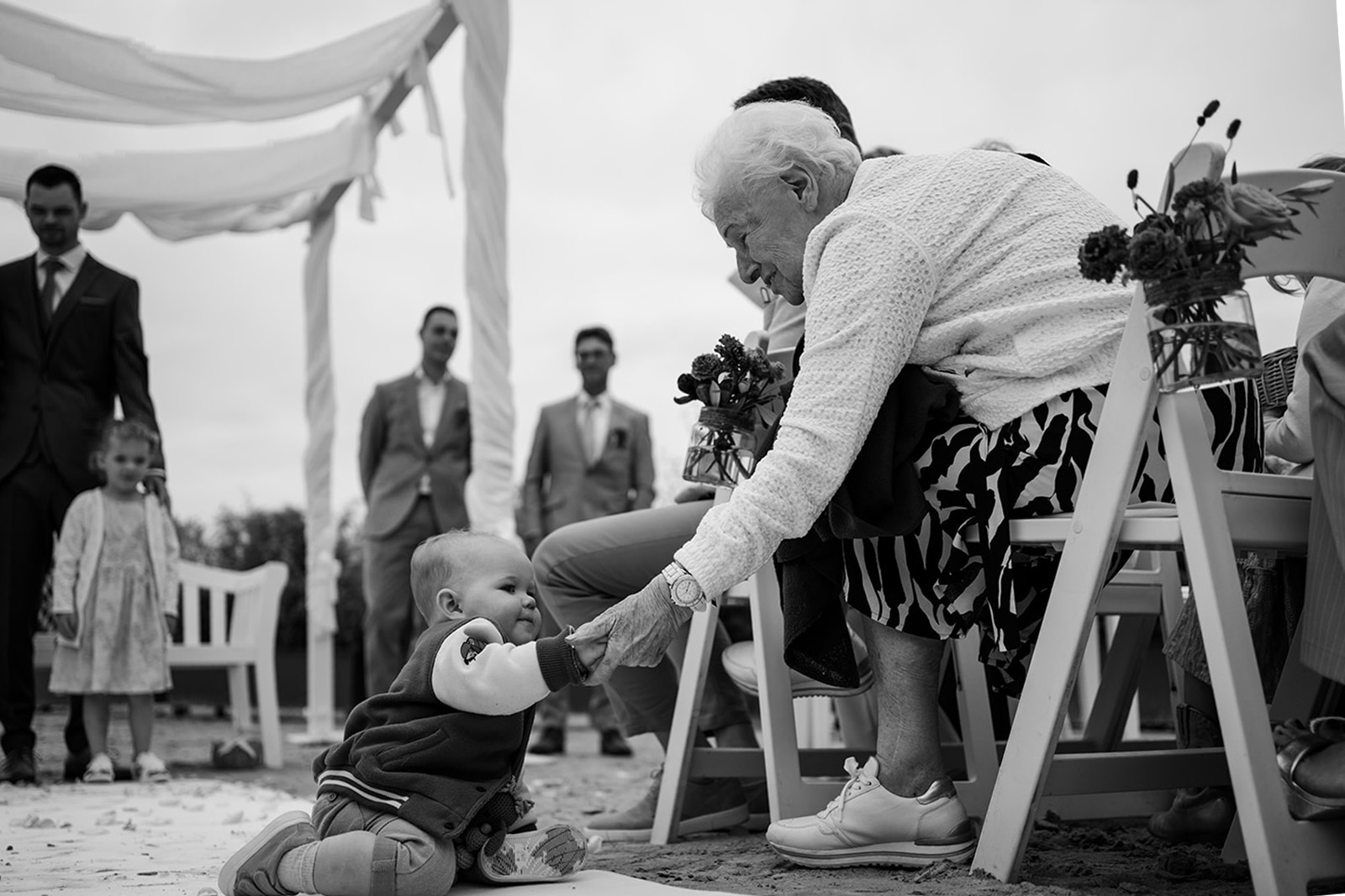 Een overgrootoma met haar achterkleinkind op een strand tijdens de bruiloft van haar kleinkind
